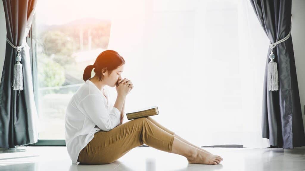 woman sitting on the floor praying with a Bible in her lap